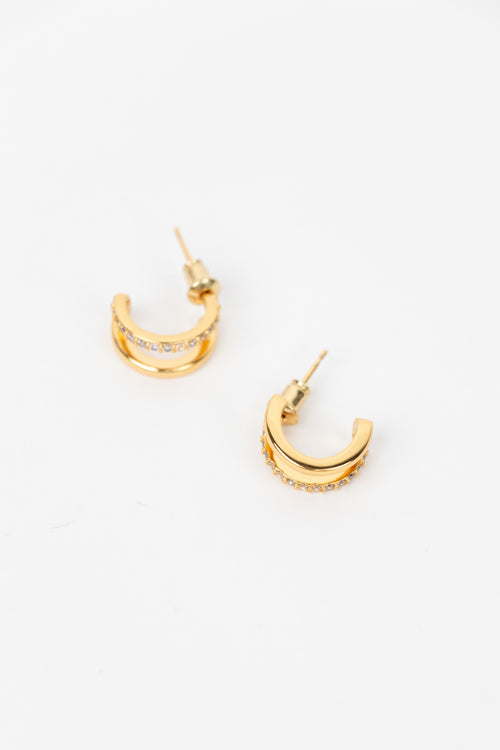 A pair of gold crescent-shaped hoop earrings with small clear stones set along the front, displayed on a clean white background.