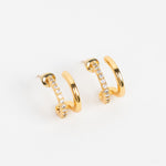 A pair of gold huggie hoop earrings with a row of small clear pavé stones on one side, displayed on a clean white background.