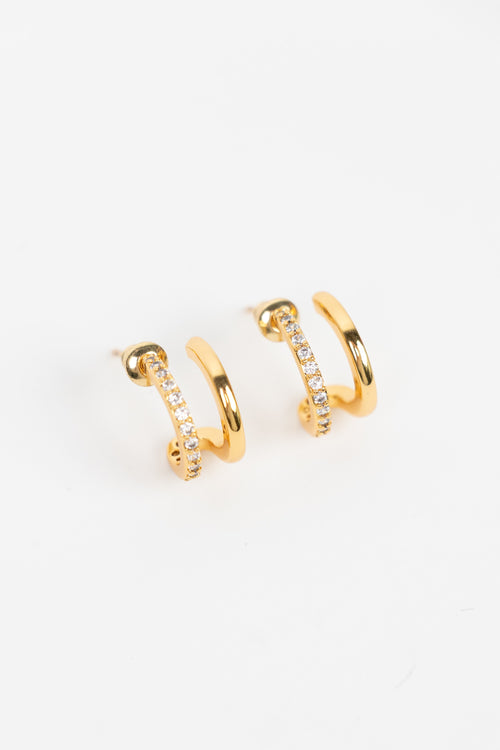 A pair of gold huggie hoop earrings with a row of small clear pavé stones on one side, displayed on a clean white background.