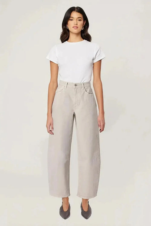 A woman modeling a white short-sleeve crewneck t-shirt and light beige wide-leg cropped trousers, paired with dark gray pointed-toe flats, against a plain off-white studio background.