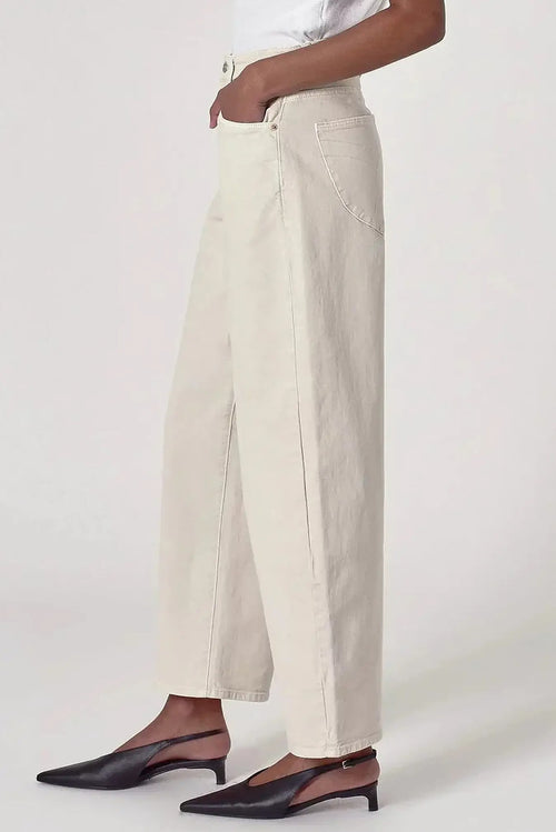 A model wearing off-white wide-leg cropped pants with a white top and black slingback mule heels, shown from the waist down against a light gray studio background.