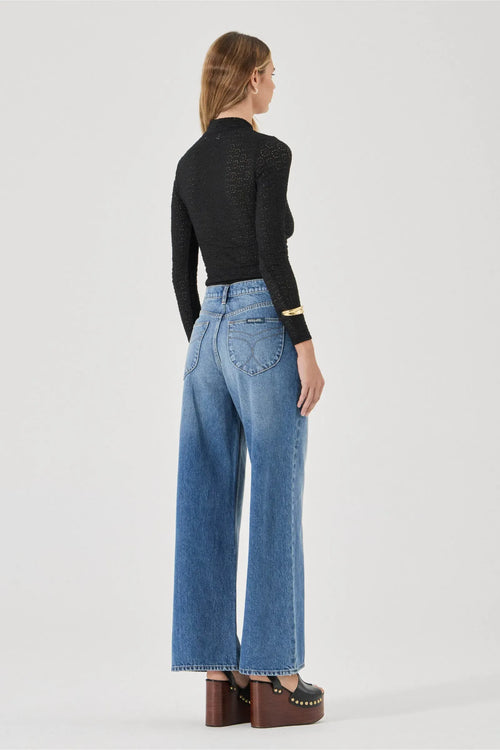 Person wearing a black top and blue jeans on a white background