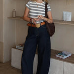 Woman standing in a room with shelves and a counter, holding a drink.