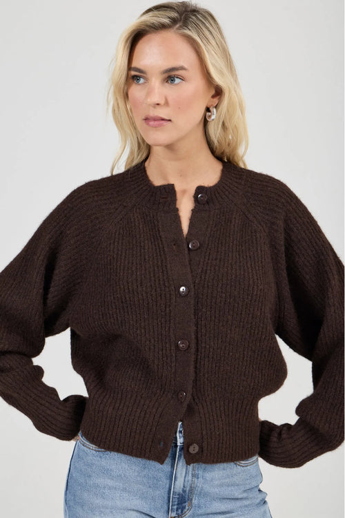Woman wearing a brown knitted cardigan and blue jeans on a plain background