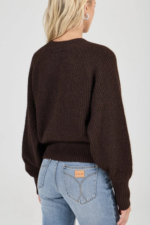 Person wearing a brown sweater and light blue jeans on a plain background