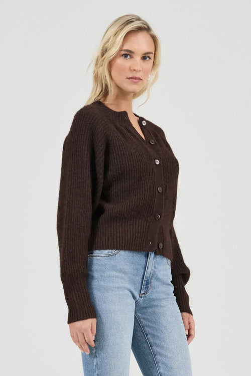 Woman wearing a brown cardigan and light blue jeans on a white background