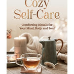 Book cover for 'Cozy Self-Care' by Sophie Golding, featuring a warm, cozy scene with a glass cup of tea, a candle, a textured metal teapot, and a knitted blanket on a wooden table.