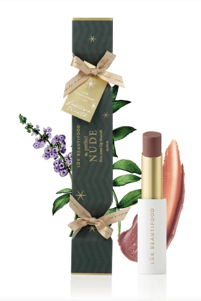 Luk Beautyfood No.06 Nude Lipstick shown with its dark green gift box decorated with gold stars, a beige ribbon, and botanical illustrations, alongside the lipstick tube and two lipstick color swatches on a white background.