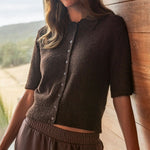 Woman in a brown outfit standing by a wooden wall with a scenic background