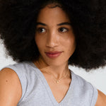 Woman with an afro wearing a gray sleeveless top against a plain background