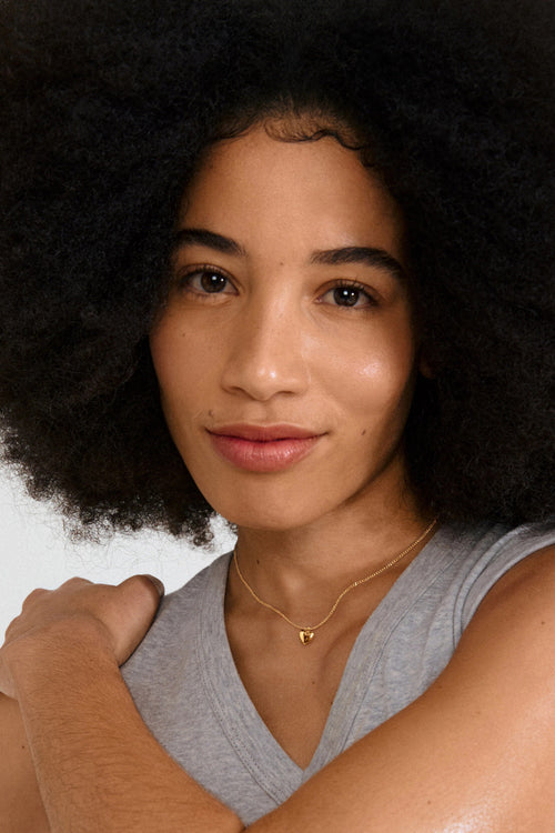 Woman with an afro hairstyle wearing a gray sleeveless top against a plain background