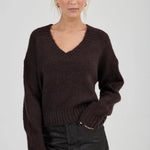 Woman wearing a brown sweater and black pants against a plain background