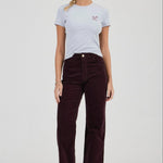 Woman wearing a light blue t-shirt and dark brown corduroy pants on a white background