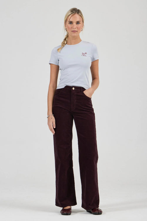 Woman wearing a light gray t-shirt and dark brown corduroy pants on a white background