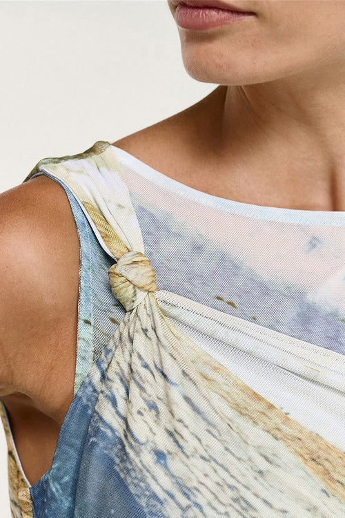 Close-up of a model wearing a one-shoulder tank top with a tie-front detail, featuring a blue, beige, and white abstract print.