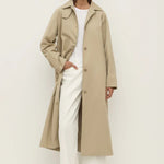 Person wearing a beige trench coat over a white outfit on a plain background