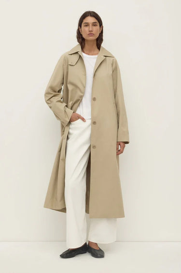 Person wearing a beige trench coat over a white outfit on a plain background