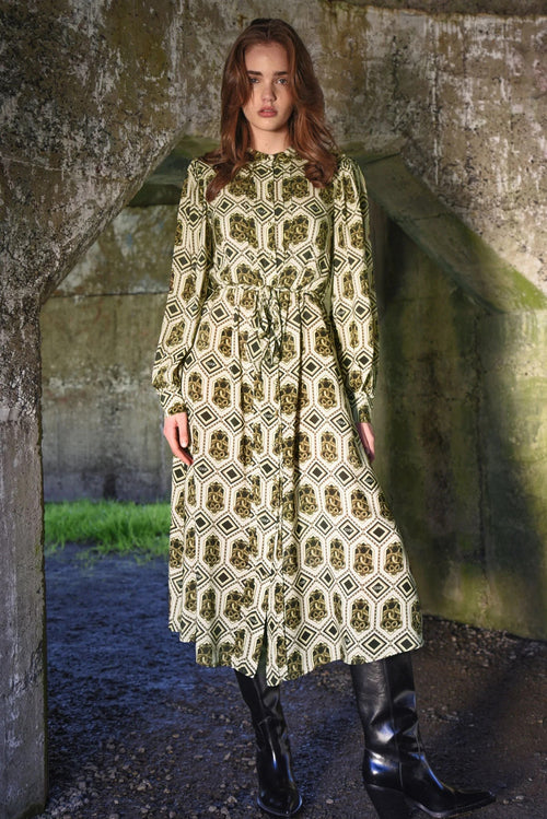 Woman wearing a patterned dress standing in front of a stone wall.