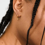 Close-up of a person wearing a gold hoop earring with braided hair against a neutral background