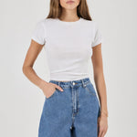 A woman modeling a white short-sleeve crewneck t-shirt and high-waisted blue denim shorts against a light gray studio background.