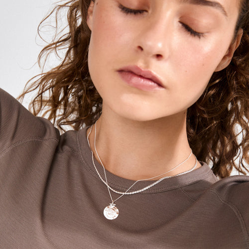 Close-up of a woman wearing a silver necklace with a pendant.