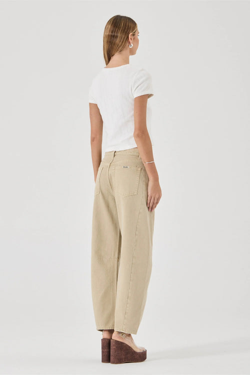 A woman shown from the back wearing a white short-sleeve t-shirt and beige wide-leg trousers, paired with brown wedge sandals, against a plain light gray studio background.