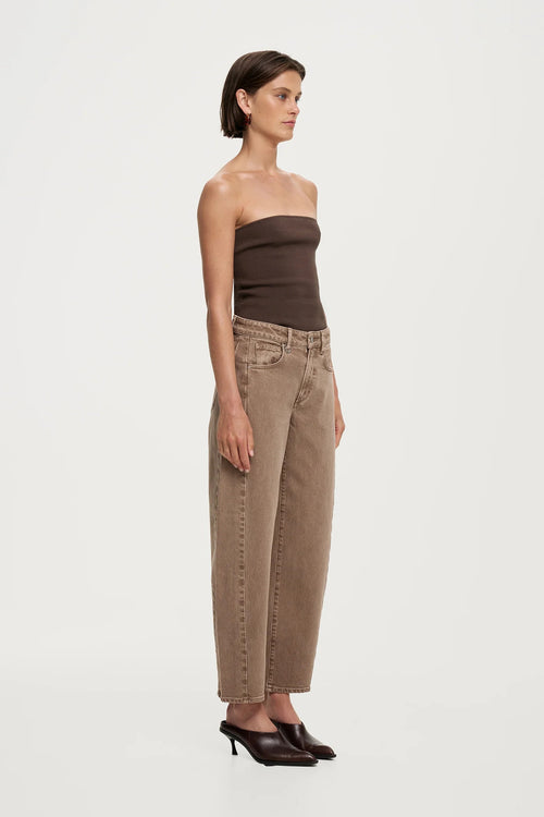A model is shown in profile wearing a dark brown strapless tube top and light brown wide-leg cropped jeans with dark brown pointed-toe heels, set against a plain light gray studio background.