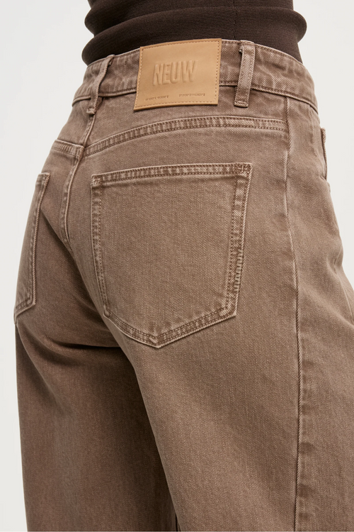Close-up of the back waist and rear pocket of a pair of brown washed denim jeans, showing a tan leather NEUN brand patch at the back waistband.