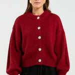 Person wearing a red cardigan with white buttons on a plain background
