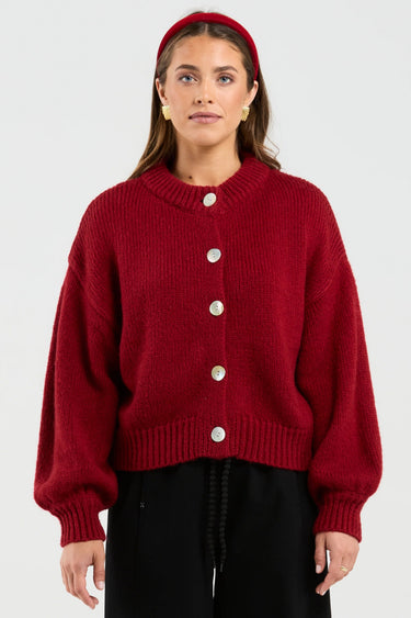 Person wearing a red cardigan with white buttons on a plain background