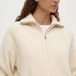 Person wearing a cream-colored zip-up sweater against a plain background