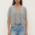 Woman wearing a gray cardigan over a gray top and blue jeans on a white background