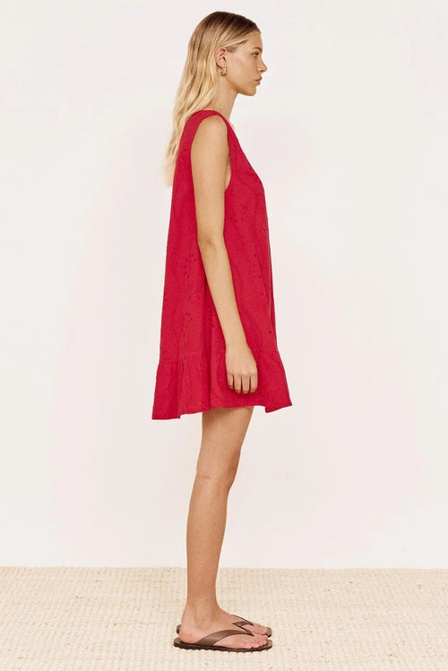 A woman stands in profile wearing a sleeveless red dress with a flared hem, paired with brown flip-flop sandals, against a plain light background.