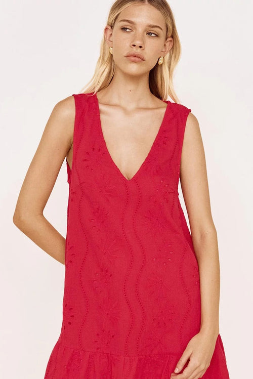 A woman modeling a sleeveless red eyelet dress with a deep V-neckline against a plain white studio background.