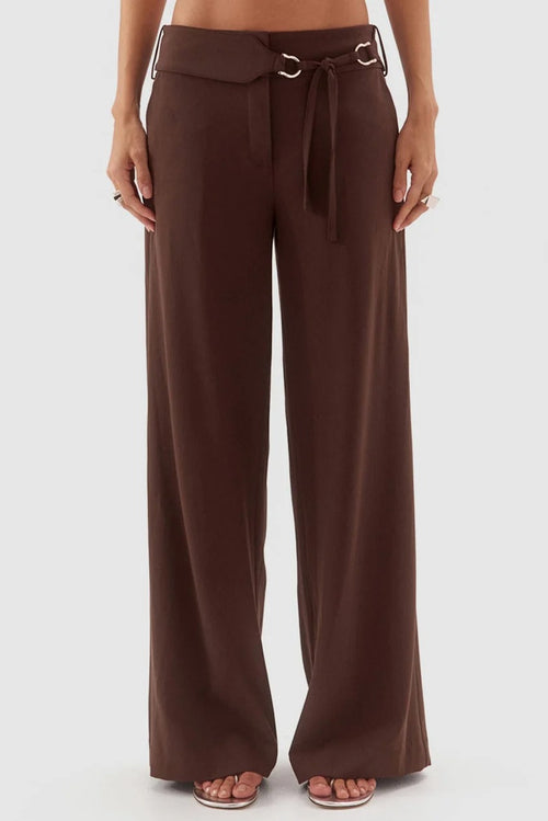 A person wearing high-waisted, wide-leg brown pants with a matching drawstring waist and silver-tone hardware, shown against a plain light gray studio background.