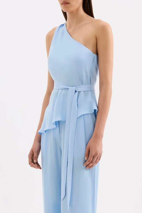 A model wearing a light blue one-shoulder jumpsuit with a matching waist tie, shown against a plain white studio background.