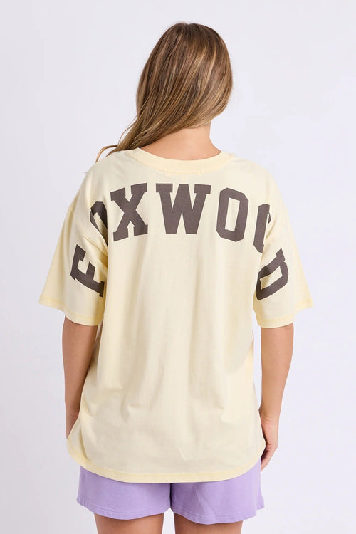 Person wearing a beige t-shirt with 'FOXWOOD' printed on the back against a white background