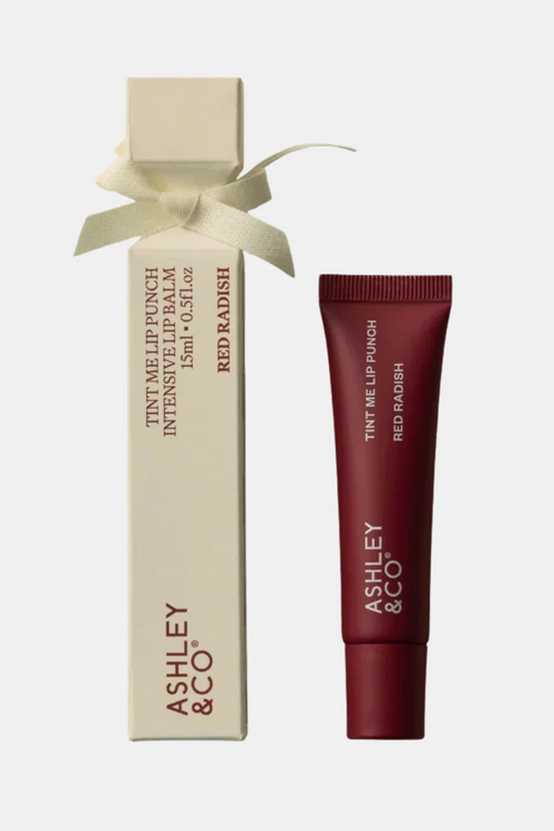 Ashley & Co Red Radish Intensive Lip Balm shown with its cream-colored box tied in a ribbon and the matching dark red lip balm tube on a light gray background.