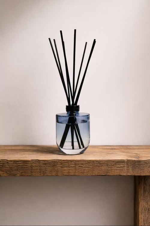 Glass diffuser with black sticks on a wooden surface against a plain background