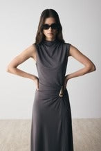 Woman wearing a gray sleeveless dress with a belt against a plain background