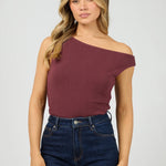 Woman wearing a burgundy one-shoulder top and blue jeans on a white background