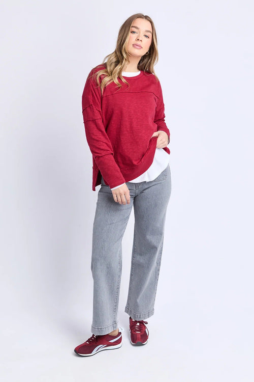 Woman wearing a red sweater, light gray jeans, and red shoes on a white background