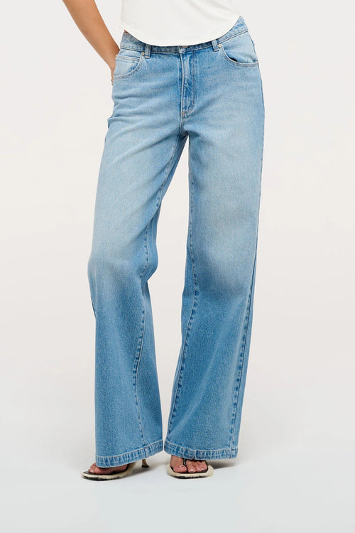 Model wearing mid indigo wide-leg jeans with a mid-rise waist, styled with a white sleeveless V-neck top and sandals.