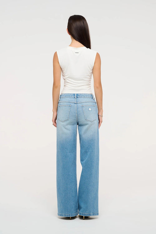 Model wearing mid indigo wide-leg jeans with a mid-rise waist, styled with a white sleeveless V-neck top and sandals.