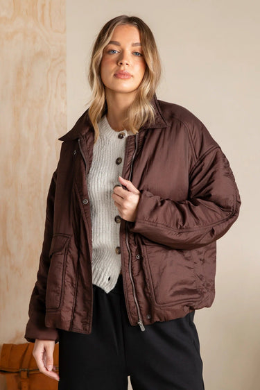 Woman wearing a brown jacket against a wooden paneled wall