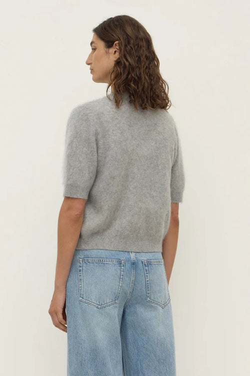 Person wearing a gray sweater and light blue jeans against a white background