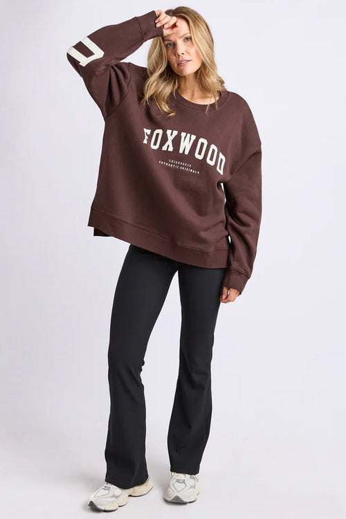 Person wearing a brown 'Foxwood' sweatshirt and black pants on a white background