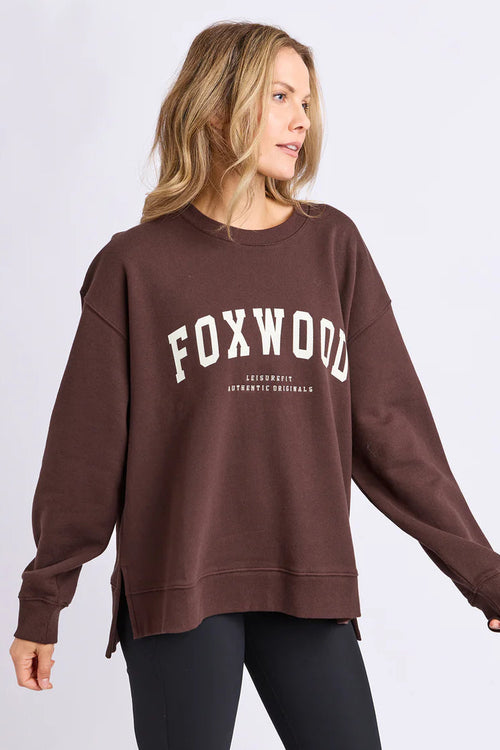 Woman wearing a brown sweatshirt with 'FOXWOOD' printed on it against a light gray background