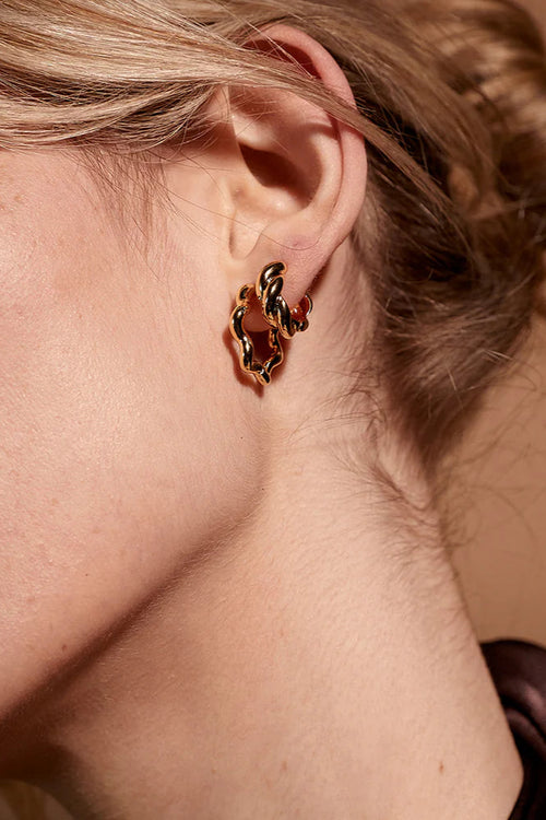Close-up of an ear wearing a gold hoop earring with a brown background