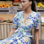 model wears and blue and orange floral maxi dress in front of a fruit stall